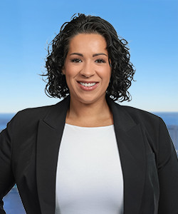 Professional woman with curly hair smiling outdoors against a blue sky.