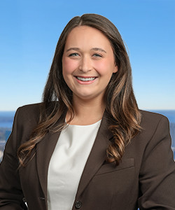 Smiling woman with long brown hair in a brown blazer and white top outdoors.