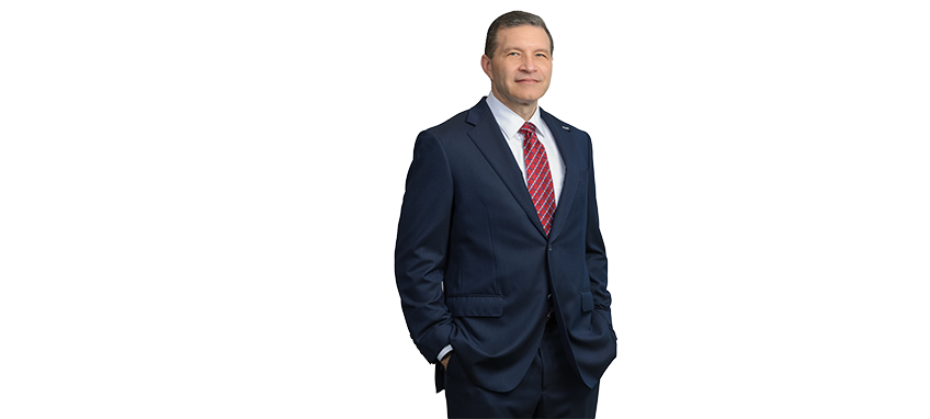 A man in a navy suit and red striped tie standing with hands in pockets.