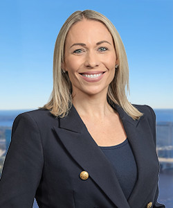 Smiling woman with blonde hair in a navy blazer outdoors.