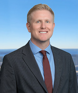 Professional portrait of a man in a suit with a blue sky background.