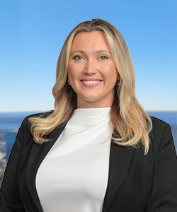 Professional woman with blonde hair smiling against a blue sky background.