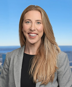 Professional woman with long blonde hair smiling outdoors against a blue sky.