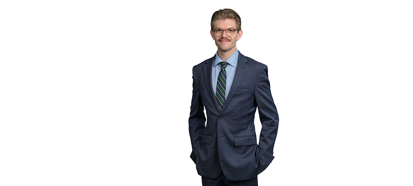 A man in a blue suit with glasses and a striped tie, smiling confidently.